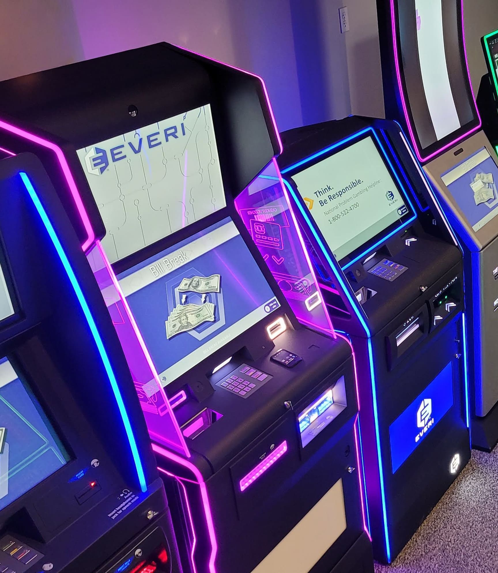 Row of EVERI-branded casino cash-access and bill-break kiosks manufactured by Nevatronix, lit with magenta and blue accent lighting