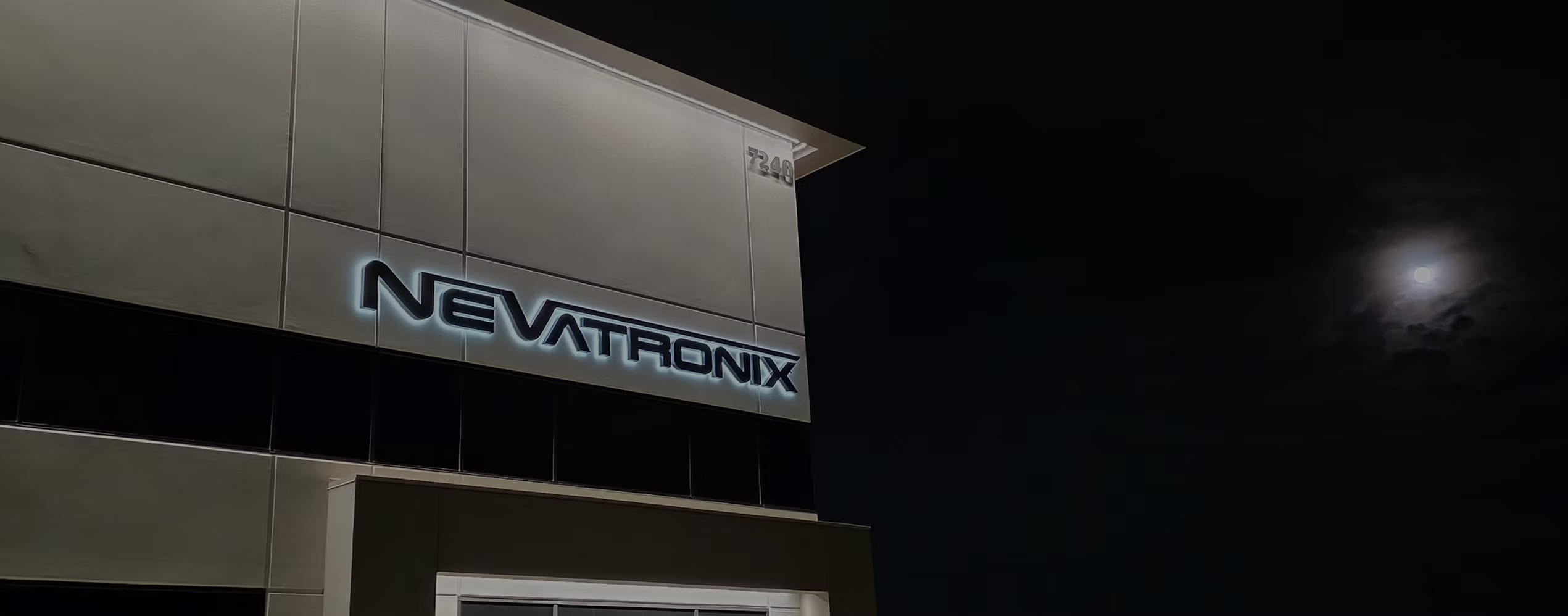 Nevatronix headquarters building exterior at night, illuminated with backlit NEVATRONIX signage under a full moon