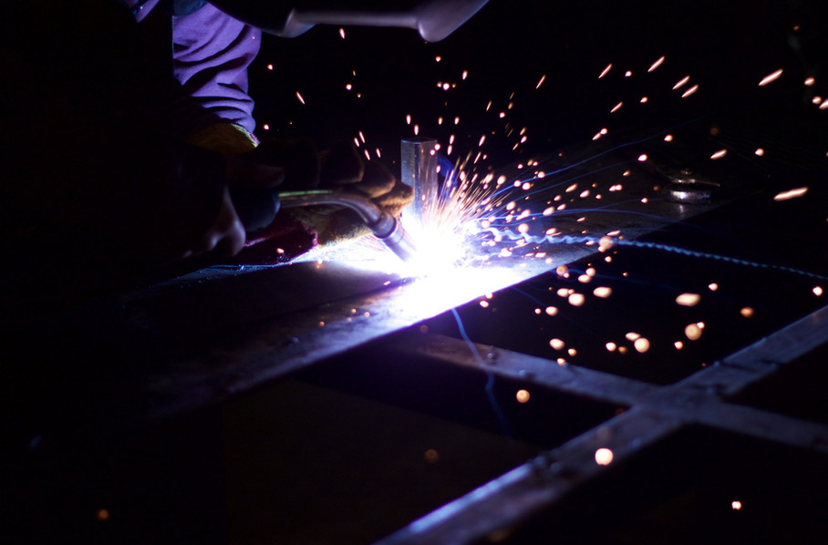 Bright shower of sparks as a technician welds a steel sheet-metal fabrication in a dark shop