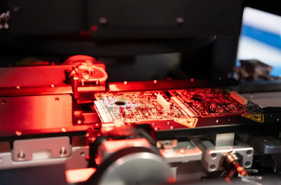 Populated printed circuit boards moving through an automated PCB assembly line under red inspection lighting