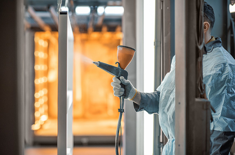 Technician in protective gear spray-applying powder coating to a part inside a coating booth